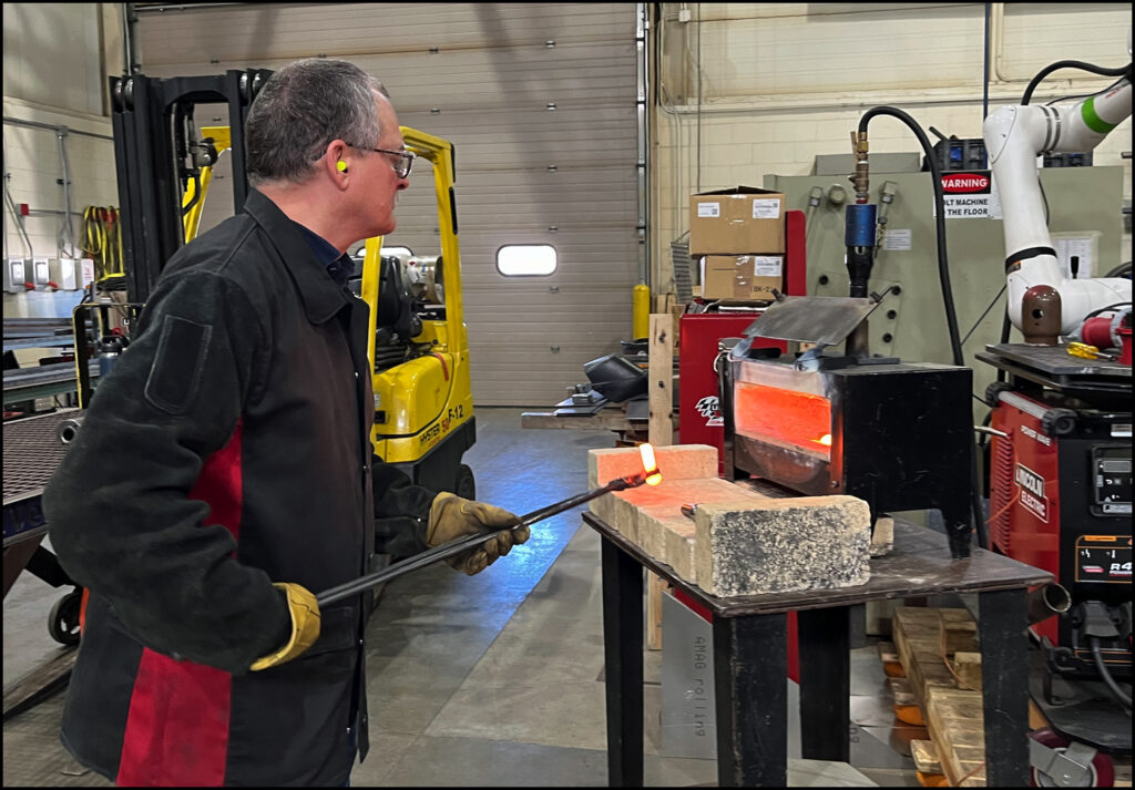Photo: Nan Jackson, 2024 Jeff Haynes, rivet heater, uses tongs fabricated by craftsman/ artist Jeff Seelye.